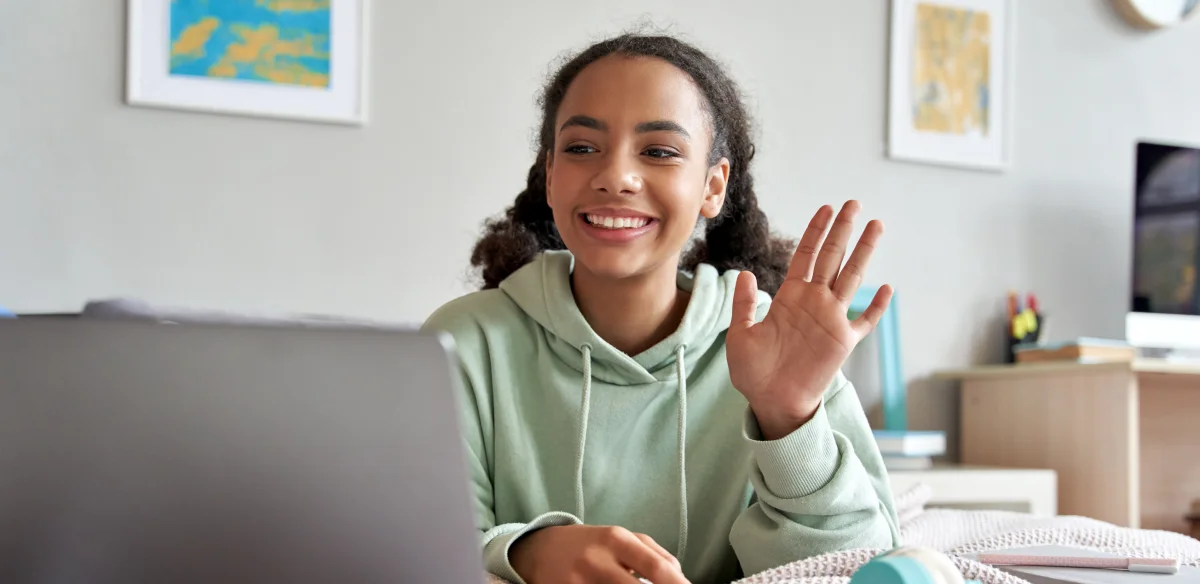 High school student waiving at ther online class wearing a light green hoodie